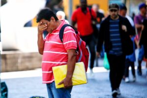 Hombre preocupado se toma la cabeza en una calle concurrida