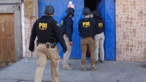 Detectives de la PDI con chalecos institucionales ingresan a un inmueble de portón azul