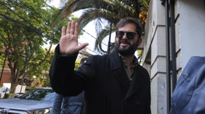 Hombre con anteojos de sol saluda con la mano al salir de un edificio