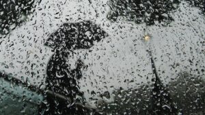 Persona con paraguas vista a través de un vidrio mojado por la lluvia